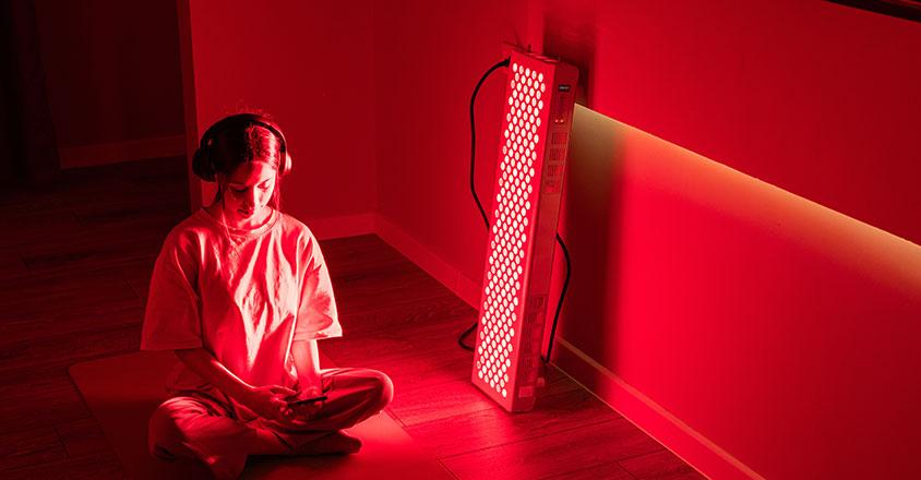 woman sitting next to a red light therapy device