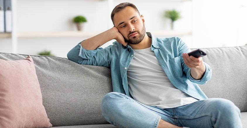 Man sitting on couch with tv remote in hand, looking bored
