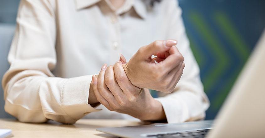 person sitting at desk holding their wrist zoomed in