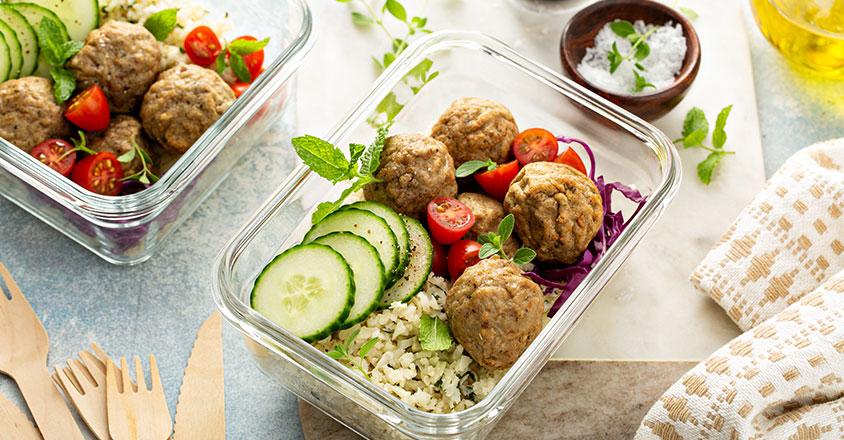 Table of healthy food options including meatballs, rice, cucumber and tomato