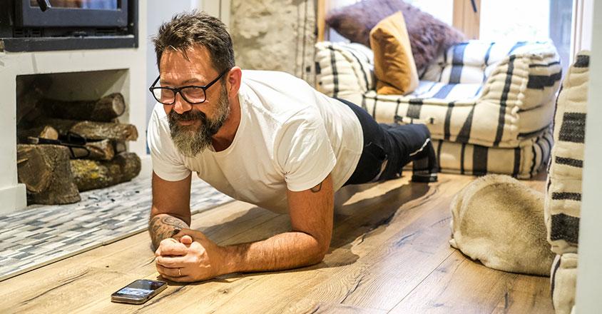 man doing a plank in his living room with dog laying near him