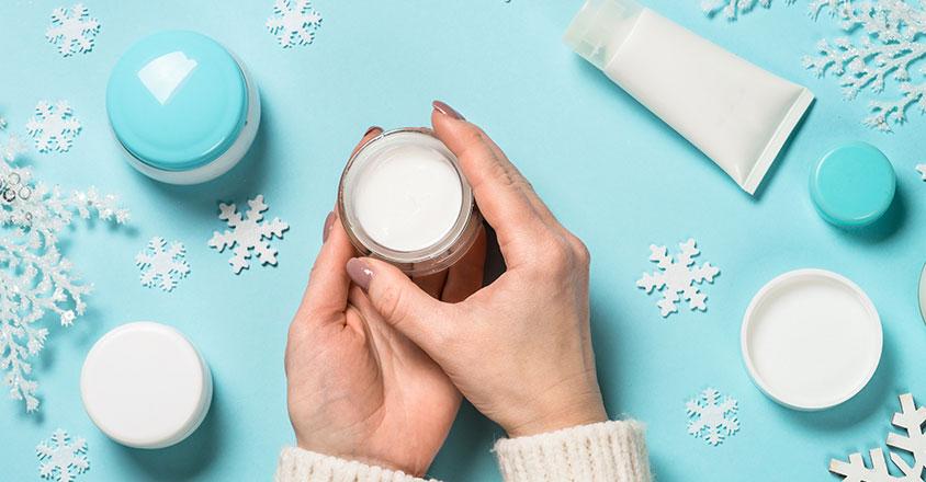 hands holding moisturizer with blue background and skincare surrounded by snowflakes