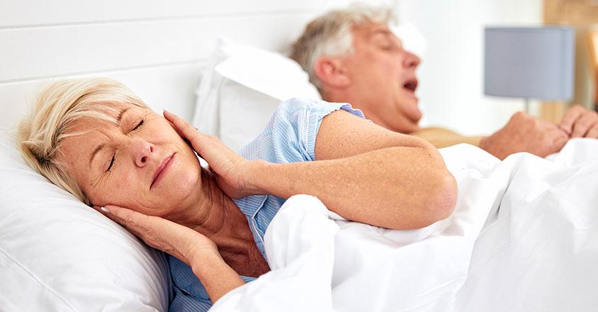 woman sleeping with ears covered by hands due to husband snoring next to her