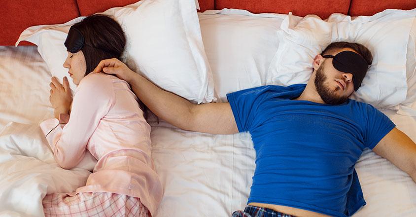 Woman sleeping on her side with man next to her sleeping on his back with arm sprawled out on top of her neck