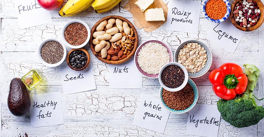 Healthy foods photographed on a table, including healthy fats, seeds, nuts, whole grains, dairy, legumes, and vegetables 