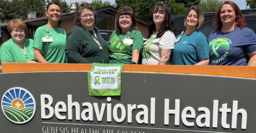 Genesis Behavioral Health sign with employees posing behind it in honor of Mental health awareness month 