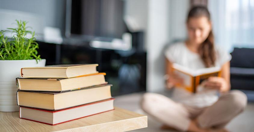 woman sitting reading a book with a stack of books on table