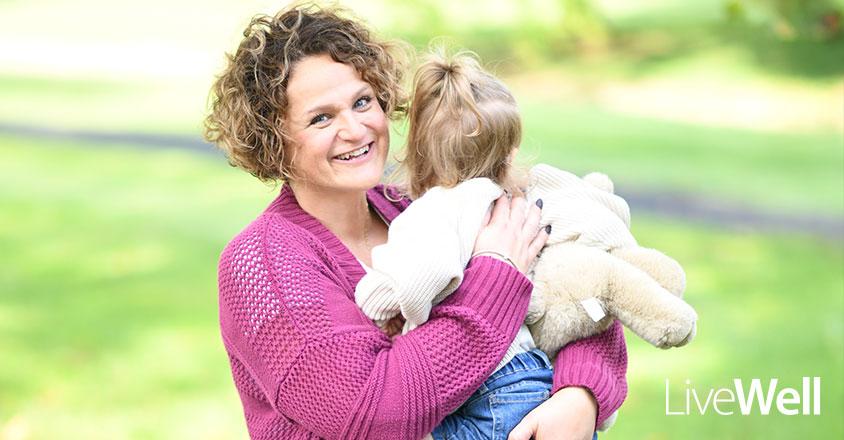 Genesis Cancer Care Center patient, Natalie Thompson, smiling with her 2 year old baby girl in her arms, in a bright setting outside