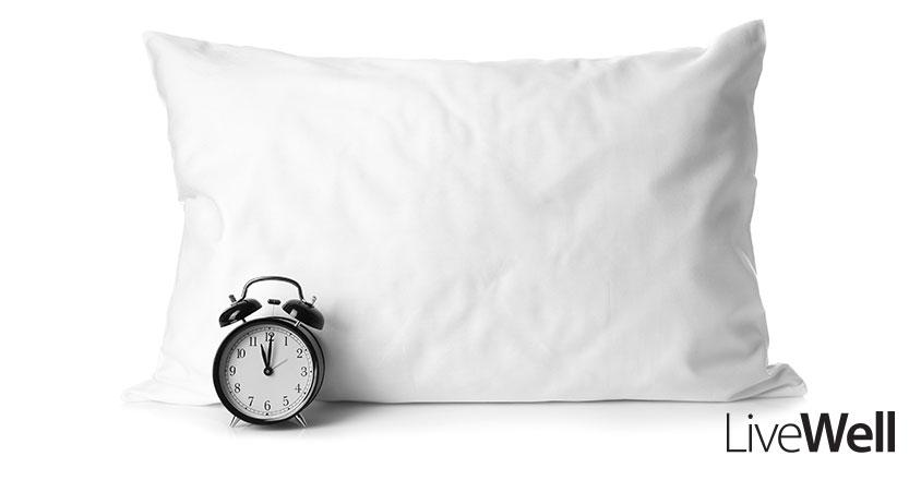 Alarm clock placed in front of pillow against a white backdrop