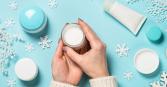 hands holding moisturizer with blue background and skincare surrounded by snowflakes