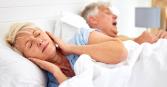 woman sleeping with ears covered by hands due to husband snoring next to her