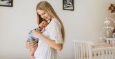 mother holding her newborn baby in nursery with crib in background