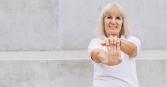 older woman stretching her wrists, smiling at camera
