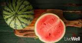 a watermelon, cut in half, sitting on top of a wood cutting board