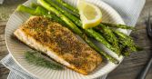 This close-up shot features a delectable grilled salmon fillet, served alongside fresh green asparagus spears and a vibrant lemon wedge. The salmon is seasoned and has a visually appealing texture. 
