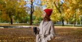 woman walking around outside on a beautiful autumn day with a warm mug in hand and bundled up in winter coat and hat