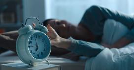 woman turning off morning alarm clock in bed