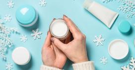 hands holding moisturizer with blue background and skincare surrounded by snowflakes