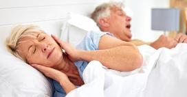 woman sleeping with ears covered by hands due to husband snoring next to her