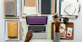 aerial photo of woman working on laptop with a busy but organized desk of files and office material