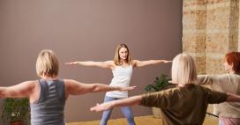 yoga instructor and class holding a pose of arms straight out to the sides and legs wide stance