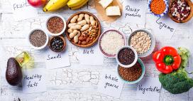 Healthy foods photographed on a table, including healthy fats, seeds, nuts, whole grains, dairy, legumes, and vegetables 