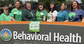 Genesis Behavioral Health sign with employees posing behind it in honor of Mental health awareness month 