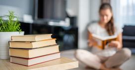 woman sitting reading a book with a stack of books on table