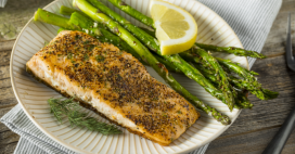 This close-up shot features a delectable grilled salmon fillet, served alongside fresh green asparagus spears and a vibrant lemon wedge. The salmon is seasoned and has a visually appealing texture. 